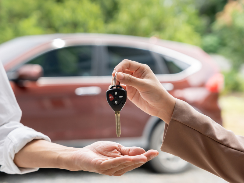 A man hands a car key to another person, symbolizing a transfer of ownership or responsibility.